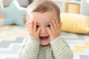 Bébé de six mois souriant en jouant au coucou-caché, illustrant le moment quand bébé commence a rire.